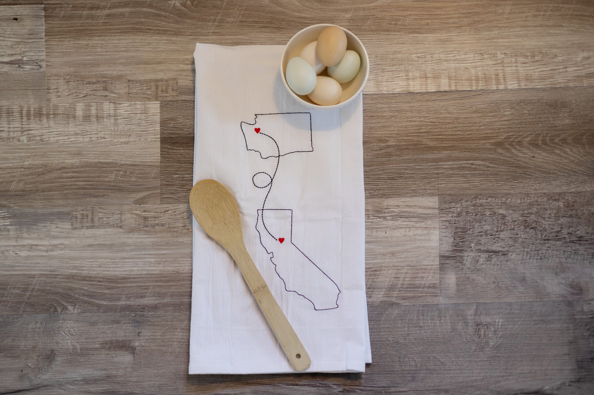 Two states embroidered on a tea towel connected by a line with hearts over cities