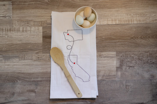 Two states embroidered on a tea towel connected by a line with hearts over cities