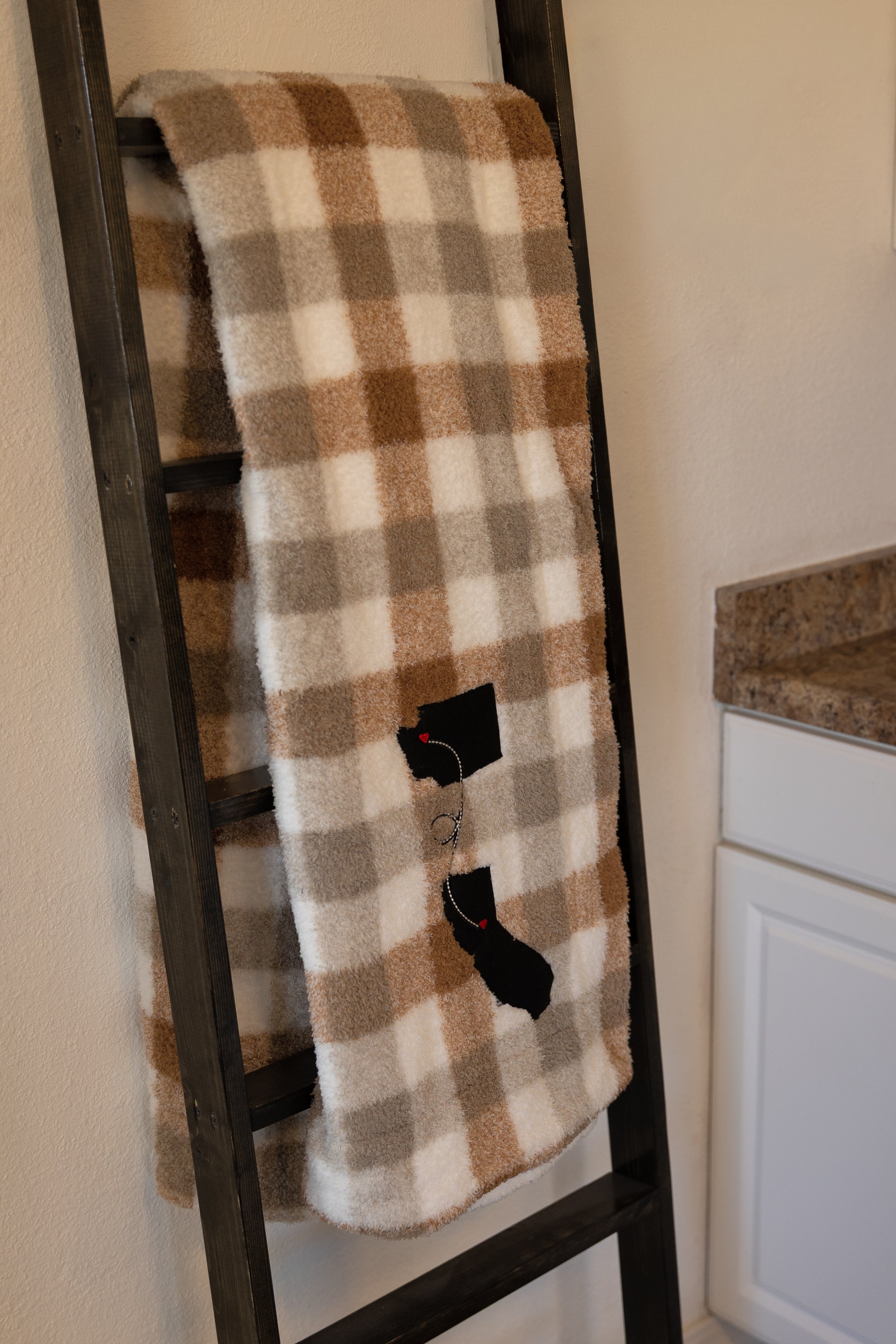 Two states appliqued on a plaid blanket connected by hearts over cities